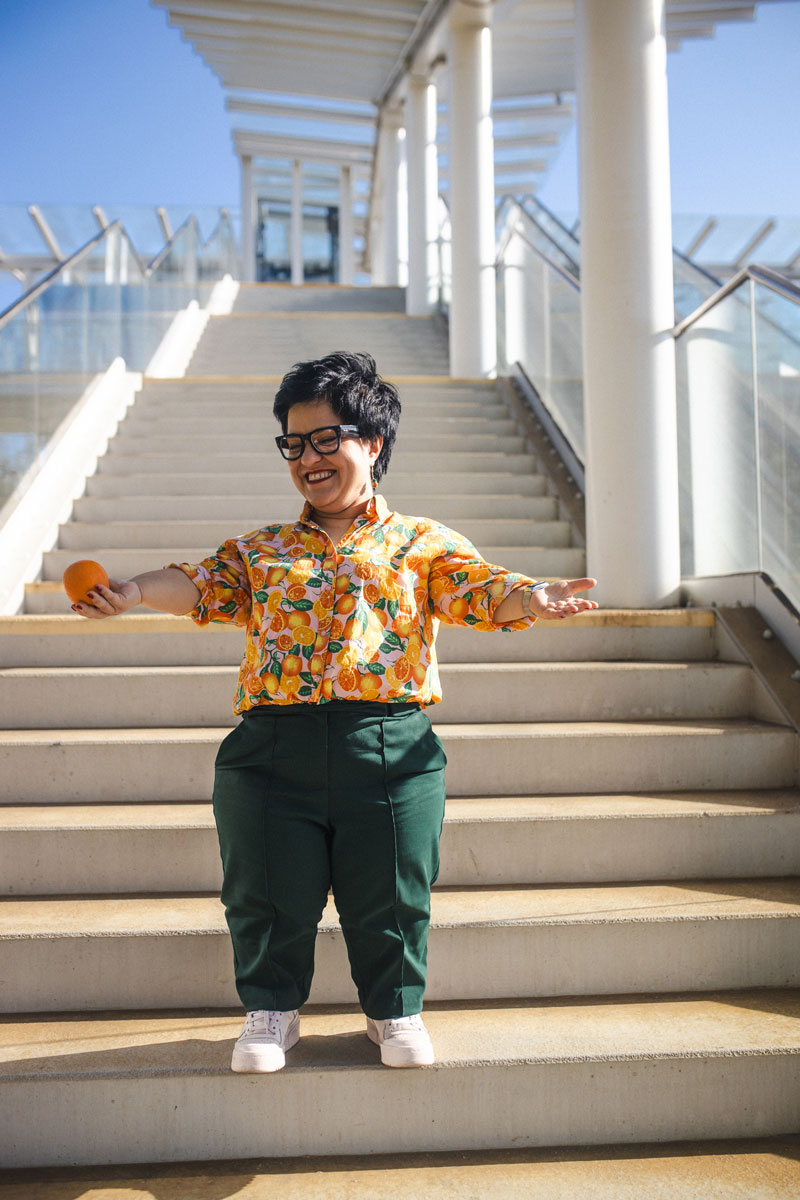 Justyna Cuże stoi na schodach z rozłożonymi rękami, trzymając pomarańczę.