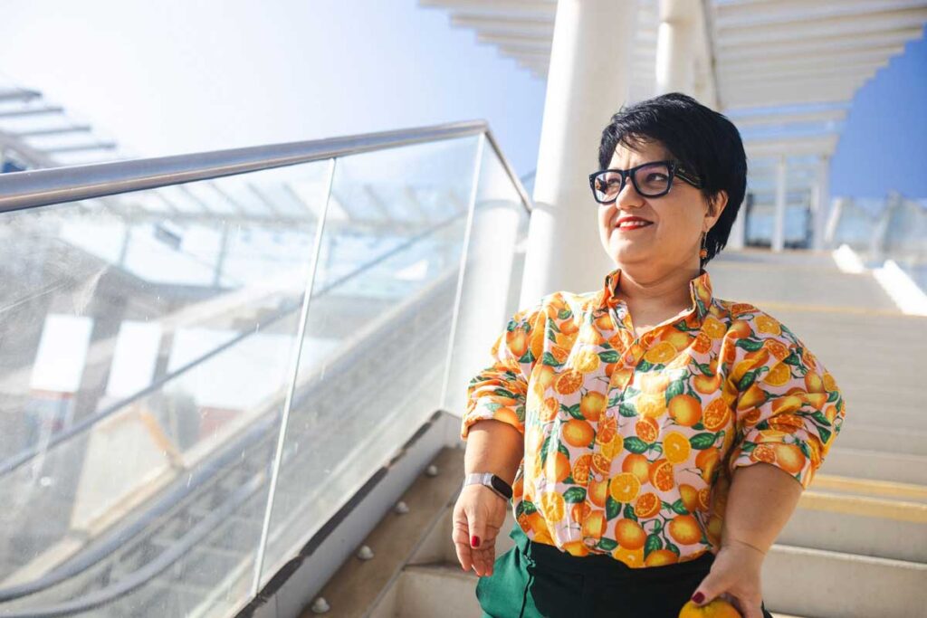 Justyna Cuże stoi na schodach z uśmiechem, trzymając pomarańczę i patrząc w bok.