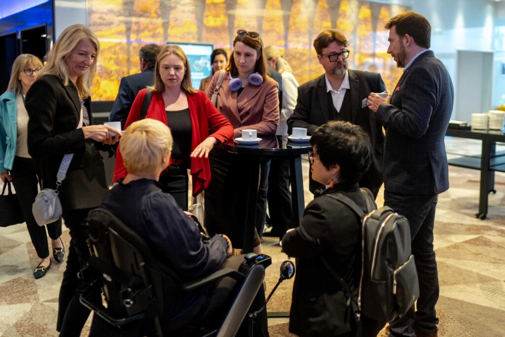 Grupa osób rozmawia przy stoliku podczas przerwy konferencyjnej; Justyna Cuże stoi po prawej stronie.