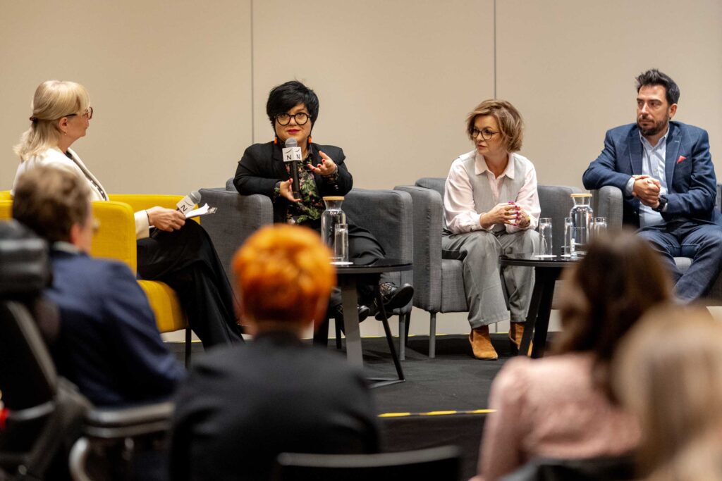 Justyna Cuże zabiera głos w panelu z trzema rozmówcami na scenie.